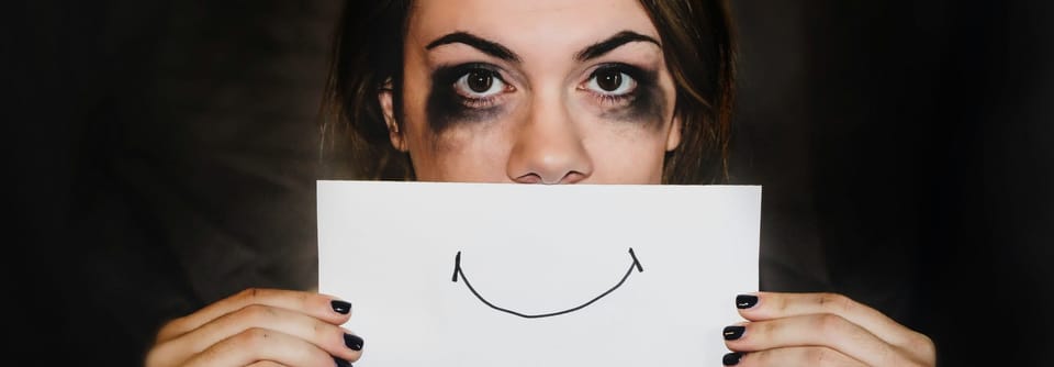 Image of a woman holding a smile drawn on paper over her mouth, clearly unhappy.